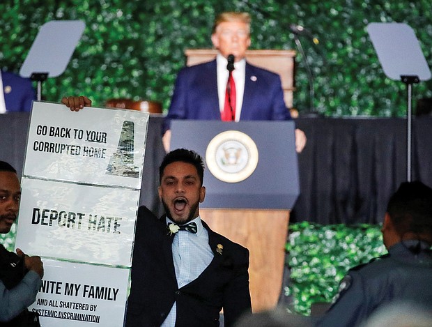 Fairfax Delegate Ibraheem Samirah unfurls a sign in protest during President Trump’s keynote speech Tuesday at the 400th anniversary commemoration in Jamestown.