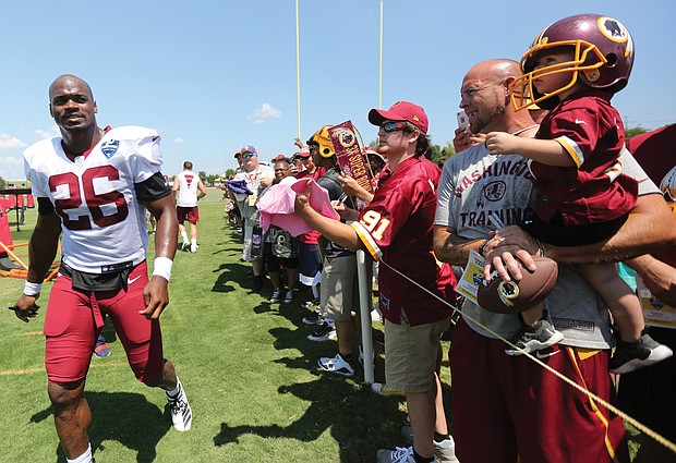 Adrian Peterson, a star running back for the Washington NFL team, strides past fans after a practice session.