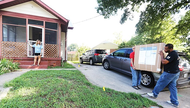 REAL LIFE founder Sarah Scarbrough waits to hold the door as Ryan Riggs, left, a case manager at the home for men in recovery, and Leander Watkins, a resident at the men’s home, carry a new bathroom vanity inside for the new women’s recovery house in South Side.