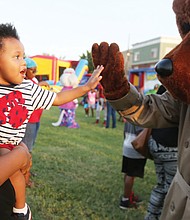 Jeremiah Jackson, 2, gives a high five to McGruff the Crime Dog from the arms of his mom, Kahdijah Overstreet, during the National Night Out event hosted Tuesday evening by Sixth Mount Zion Baptist Church in Jackson Ward.