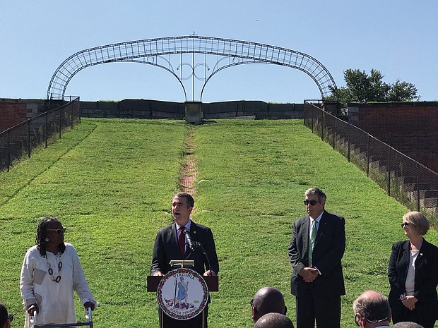 Gov. Ralph S. Northam speaks at a news conference Tuesday in front of the 50-foot memorial arch at Fort Monroe, showing that the letters honoring Confederate president Jefferson Davis have been removed. With the governor are, from left, state Sen. Mamie Locke of Hampton; Glenn Oder, executive director of the Fort Monroe Authority; and Molly J. Ward, former state secretary of natural resources and a former trustee of the authority.
