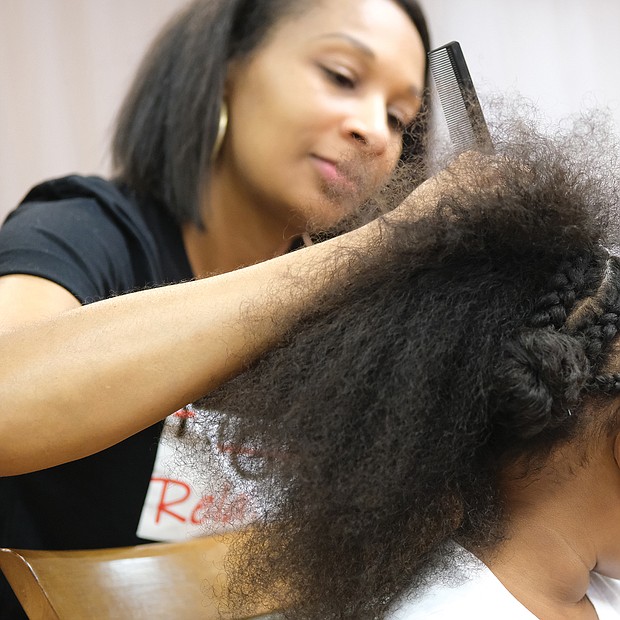 Coordinator of the event, Monique Brown, braids the hair of Nyla-Marie Outlaw, 6.