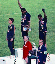Tommie Smith (center) and John Carlos (right) showing the raised fist on the podium after the 200 m race at the 1968 Summer Olympics; both wear Olympic Project for Human Rights badges. Peter Norman (silver medalist, left) from Australia also wears an OPHR badge in solidarity with Smith and Carlos.