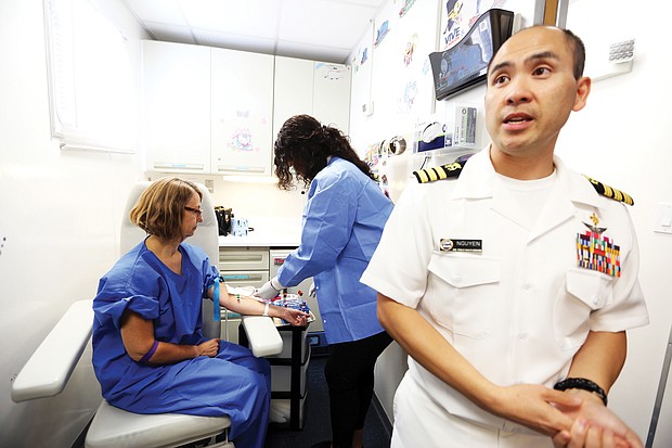 Dr. Duong “Tony” Nguyen shows the inside of one of the mobile examination centers, where various rooms are set up for specific tests. In this unit, the blood lab, phlebotomist Adraiannah Dobson shows the media how blood is drawn from Susan Lukacs, a worker with the Centers for Disease Control.