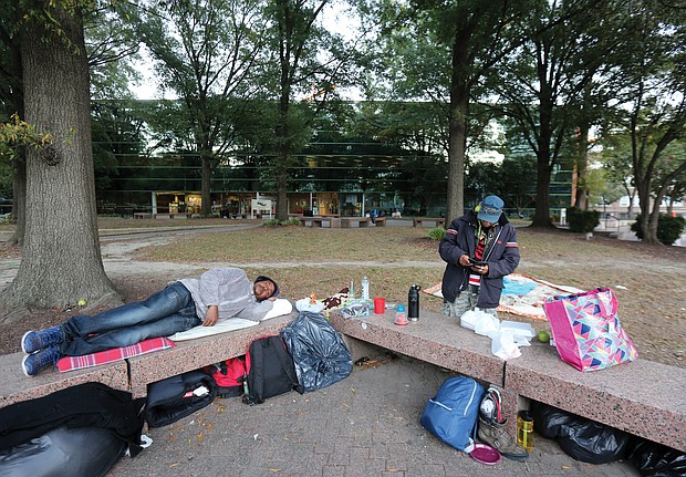 Burney Hatchett III, left, and Kolap Limm arrange their temporary sleeping quarters on benches in the plaza in front of the city Department of Social Services building at 9th and Marshall streets in Downtown on Oct. 18. The two men are among the four to 10 homeless individuals who have taken to sleeping nightly in the plaza across from City Hall. The city operates a cold weather shelter, but officials said the weather has been too warm to open it.