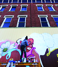 Cityscape: Slices of life and scenes in Richmond-Artist Austin Miles of Petersburg puts the finishing touches last week on this new mural that now decorates Max Market, 1125 Hull St. She is contributing the fine details to the mural that began with a community paint day Oct. 5. The mural is the first of a planned series titled “Brown Girl Narratives” that Kristal Brown, founder and leader of Black Women Cache LLC, is spearheading. This and other murals will help fulfill the goal of the organization, Ms. Brown said, which is “to highlight the lived experiences of black women through media and visual arts.” Next year, the Virginia Commonwealth University doctoral student plans to release a coffee table book focusing on black women and hold other events. (Regina H. Boone/Richmond Free Press)