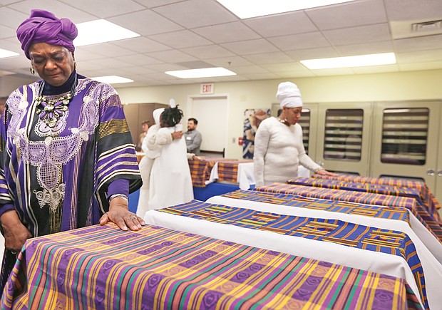 Richmond Delegate Delores L. McQuinn, a minister and chair of the Richmond Slave Trail Commission, prayerfully puts her hand on the Kente cloth covering one of 17 boxes of human remains found in 1994 in a well on Virginia Commonwealth University’s medical campus. The remains, which were returned to Richmond during a ceremony on Monday, will be stored by the state Department of Historic Resources while planning for an appropriate burial and memorial continues.