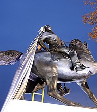 Kehinde Wiley’s “Rumors of War” sculpture stands partially revealed outside the Virginia Museum of Fine Arts as Richmond Firefighter John Lukhard works to remove the drape caught on the figure’s hair during Tuesday’s unveiling ceremony. Right, artist Kehinde Wiley, 42, enthusiastically heads to the microphone to address the throngs of people awaiting the unveiling of the sculpture funded by private donations.