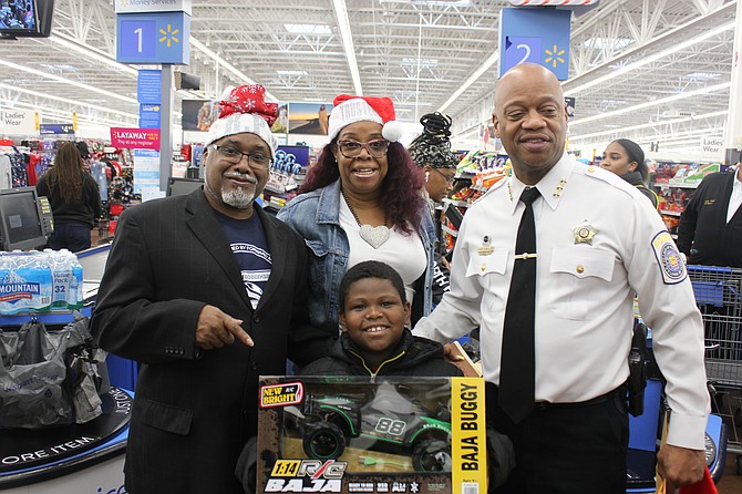 (from left) Robbins Mayor Tyrone Ward, Robbins Trustee Jacquelyn Henry and Robbins Police Chief Roy Williams Sr. happily stood with an elementary student from Robbins, who participated in the Shop with a Cop Christmas program sponsored by the Village of Robbins and its police department. Photo credit: By Wendell Hutson
