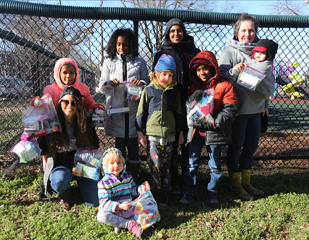 Ashley Smith-O’Meara, seated left, wants people to feel free to receive help without judgment or condition. She and other parents and children from the FERNNS Homeschool Co-op volunteering with the Walls of Love project in Richmond show off bags packed with personal items that will be put on the fence at Abner Clay Park in Jackson Ward. With her are, standing from left, her daughter, Sofia Ruffin, 9; Asfana Dawkins, 9; parent Umerah Mujahid; Sam Outland-Brock, 7; Jahid Dawkins, 8; parent Joy Outland-Brock holding her year-old daughter, Florence Outland-Brock; and seated front, Felicity Outland-Brock, 4.