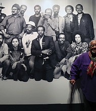 Shawn Walker, who was a member of the Kamoinge collective established by the late Henrico County native Louis Draper in New York City in 1963, stands in front of a historic photo of the group,  The exhibit will be on view through June 14 at the museum, 200 N. Arthur Ashe Blvd.