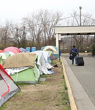 A resident of Cathy’s Camp on Oliver Hill Way rolls his belongings next to a row of tents. To the right is the Annie Giles Community Resource Center, the city’s winter shelter. The center also was open during the day this week for residents to meet with staff from nonprofits, the city and a mental health agency as part of an outreach effort to help provide needed services.