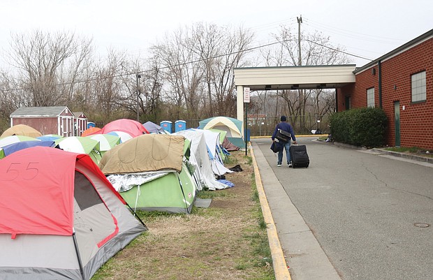 A resident of Cathy’s Camp on Oliver Hill Way rolls his belongings next to a row of tents. To the right is the Annie Giles Community Resource Center, the city’s winter shelter. The center also was open during the day this week for residents to meet with staff from nonprofits, the city and a mental health agency as part of an outreach effort to help provide needed services.