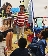 Virginia First Lady Pam Northam, laden with a bag full of show-and-tell items, settles in to read “When Spring Comes” to kindergartners at Overby-Sheppard Elementary School in Highland Park on Monday during the annual Read Across America Day. She is helped by Jahmir Johnson, who dons bumble bee wings and antennae to illustrate signs of the coming spring.