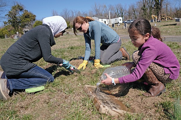 Tessneem Khalil, 7, right, helps uncover gravestones in the 104-year-old Woodland Cemetery in Henrico County. She is working with her mother, left, Rania Fetouh, and Kathleen Harrell, her teacher at Shady Grove Elementary School in Henrico County. Ms. Harrell has volunteered consistently on Sunday afternoons with Dr. John W.J. “Bill” Slavin to improve the neglected burial ground best known as the last resting place of Arthur Ashe Jr., the Richmond native who earned international renown in tennis and as a humanitarian.