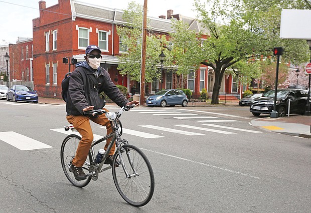 A man rides his bicycle through Jackson Ward on Tuesday wearing a medical mask as an extra precaution during the continuing spread of COVID-19 in Virginia.