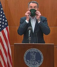 Gov. Ralph S. Northam puts on a mask during a media briefing on Monday that was made by inmates in the state Department of Corrections. The demonstration was to remind Virginians to cover their noses and mouths when they go out in public to help stop the spread of COVID-19.