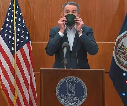 Gov. Ralph S. Northam puts on a mask during a media briefing on Monday that was made by inmates in the state Department of Corrections. The demonstration was to remind Virginians to cover their noses and mouths when they go out in public to help stop the spread of COVID-19.