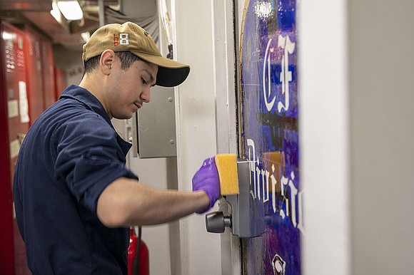 Information Systems Technician 3rd Class Ricardo Trevino, from Houston, scrubs a door handle with HTH (bleach) aboard the amphibious assault …