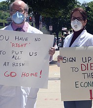 Dr. Erich Bruhn, a general surgeon from Winchester, and his wife, Kristin Bruhn, a nurse who works in her husband’s practice, wear masks as they walk among protesters on Broad Street in Downtown with their own message of safety against the virus.