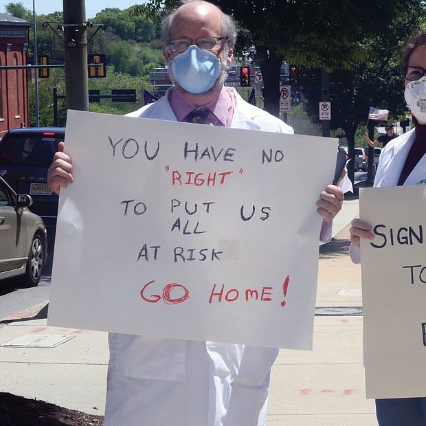 Dr. Erich Bruhn, a general surgeon from Winchester, and his wife, Kristin Bruhn, a nurse who works in her husband’s practice, wear masks as they walk among protesters on Broad Street in Downtown with their own message of safety against the virus.