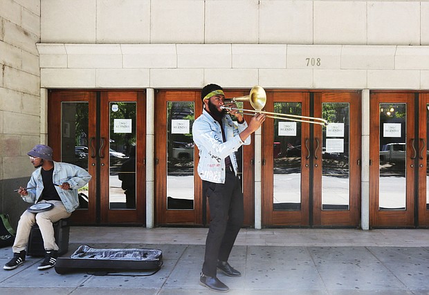 Isaiah “Prince Trombone” Robinson serenades passing motorists as fellow musician, Robert Johnson III, accompanies him on an electric drum outside The National in the 700 block of East Broad Street. The venue currently is closed because of the coronavirus. The two 23- year-old musicians began their impromptu concerts after they were laid off from their full-time gigs. Their goal: To deliver some upbeat sounds to counter the pandemic’s gloom and to possibly earn some spare change from the few pedestrians in Downtown. Other in Richmond musicians have been sharing their talents on their porches or in parks. One example is saxophonist James “Plunky” Branch, who regularly turns his porch into a solo concert platform for those within earshot in his West End neighborhood.