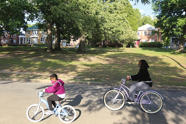 Malea Claud, 7, and her mother, Melissa Claud, regularly finish their day with a leisurely bike ride around Byrd Park. Here, they are riding Tuesday near Swan Lake. Ms. Claud reminded her daughter to secure her mask before they took off in the evening breeze.