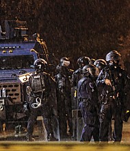 State Police in riot gear stand near an armored vehicle in front of Richmond Police headquarters at Jefferson and Grace streets Tuesday.