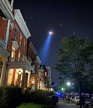 Front porch lights along Monument Avenue offer a glimpse of the crowd around the J.E.B. Stuart statue around 9 p.m. Sunday. The gathering included people trying to topple the statue.