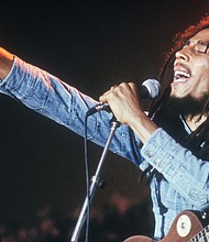 Jamaican Reggae musician, songwriter, and singer Bob Marley performs on stage, in a concert at Grona Lund, Stockholm, Sweden. He extends his fist as he sings into the microphone, with an electric guitar./Credit:	Hulton Archive/Archive Photos/Getty Images