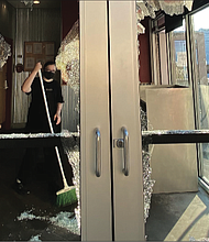 A worker at Chipotle Mexican Grill, 810 W. Grace St., sweeps up broken glass Sunday morning. The windows were shattered during a wave of vandalism that began late Saturday and continued into early Sunday.