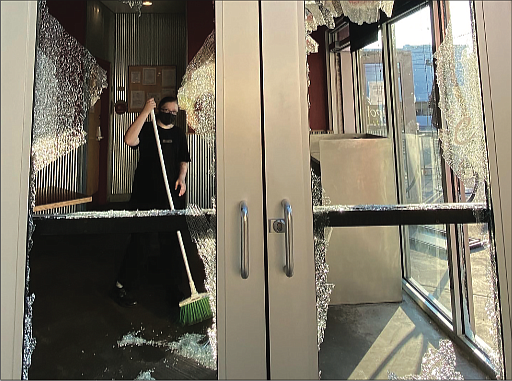 A worker at Chipotle Mexican Grill, 810 W. Grace St., sweeps up broken glass Sunday morning. The windows were shattered during a wave of vandalism that began late Saturday and continued into early Sunday.