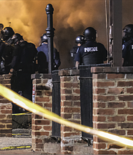 Smoke from a burning dump truck rises with tear gas in front of police officers gathered at Madison and Grace streets to protect the city police headquarters.