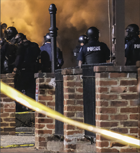 Smoke from a burning dump truck rises with tear gas in front of police officers gathered at Madison and Grace streets to protect the city police headquarters.