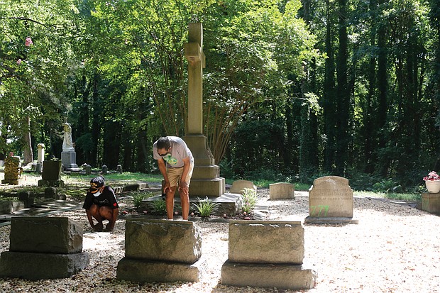 Dr. Johnny Mickens III, right, the great-grandson of Maggie L. Walker, and his daughter, Liza Mickens, survey the damage Monday morning at Mrs. Walker’s gravesite in historic Evergreen Cemetery. The back of the headstone, entrances to the gravesite and benches around the gravesite were spraypainted with “777,” numbers that are linked to white supremacist groups.