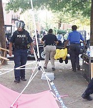 Richmond Police officers remove belongings on July 30 from “Grace Park,” a two-month-old encampment created by protesters, after residents of the area complained. Location: The grassy median at Allen Avenue
and Grace Street north of the Lee statue on Monument Avenue. On the same day, police also cleared a similar camp on the Monument Avenue median north of the camp. Two people were arrested. By Monday, activists were once again distributing food, water and literature from tables in the Allen Avenue medians. Participants said police officers were regularly checking, but mostly appeared to condone the activity. However, they said police issued warnings against overnight stays on the medians. Police reported that about 11:15 p.m. July 30, shots were fired into a vehicle near the Lee statue circle following an altercation and that the glass
door of a residence in the 1600 block of Monument Avenue had been shattered by reported gunfire. Officers canvassing the area found a rifle and ammunition magazines. “Gunfire and violent behavior is not peaceful, nonviolent protest; it is criminal, unacceptable and will not be tolerated in our city,” Richmond Police Chief Gerald M. Smith said in a statement. “The City of Richmond will take all necessary steps to protect residents and visitors and preserve peace and public safety in our communities.”
