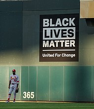 Dexter Fowler #25 of the St. Louis Cardinals looks on in front of a a wall graphic for Black Lives Matter against the Minnesota Twins on July 28, 2020 at the Target Field in Minneapolis, Minnesota. Dozens of Black baseball players will donate their salaries from Thursday and Friday to support racial justice initiatives, in honor of Jackie Robinson Day and in protest of Jacob Blake's shooting by police./Credit:	Brace Hemmelgarn/Getty Images