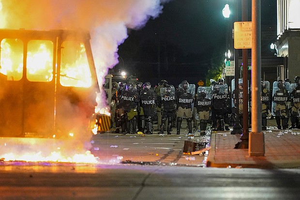 Police stand near a garbage truck ablaze during protests, Monday, Aug. 24, 2020, in Kenosha, Wis., sparked by the shooting of Jacob Blake by a Kenosha Police officer a day earlier. Officials in Kenosha, Wisconsin, enforced their curfew selectively, targeting demonstrators protesting police brutality while allowing "militia members" and supporters of law enforcement to roam the street, a federal lawsuit alleges./Credit:	Morry Gash/AP