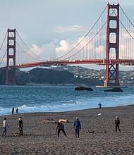 People walk at Baker Beach in March as the Golden Gate Bridge stands in the background in San Francisco./Credit:	David Paul Morris/Bloomberg/Getty Images
