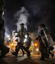 Police officers move past Louisville City Hall on Sept. 23 as a curfew is implemented at 9pm to disperse protesters after a grand jury voted to indict one of three white police officers for wanton endangerment in the death of Breonna Taylor, who was shot dead by police in her apartment, in Louisville, Kentucky./Credit:	Carlos Barria/Reuters
