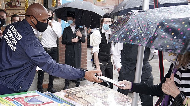 Brooklyn Borough President Eric Adams hands out a mask Tuesday./Credit:	Carlo Allegri/Reuters