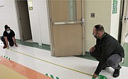 Staff measure the distance to place markers down in the hallway in one  of the schools in Plainfield Community Consolidated School District 202 to promote social distancing.