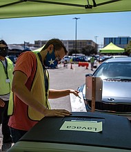 A worker wearing a protective mask puts a ballot into a secure box at a drive-thru mail ballot hand delivery center in Austin, Texas on October 2, 2020.
Credit:	Sergio Flores/Bloomberg/Getty Images