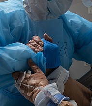 A medical staff member grabs a hand of a patient to reposition the bed in the COVID-19 intensive care unit at the United Memorial Medical Center on October 31, 2020 in Houston, Texas./Credit:	Go Nakamura/Getty Images