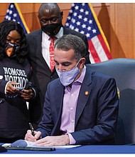 Bianca Austin, aunt of 26-year-old breonna Taylor who was killed by Louisville, Ky., police inside her apartment in March, watches as Gov. Ralph S. Northam signs a bill Monday banning no-knock warrants in Virginia. With her is the Taylor family’s lawyer, benjamin Crump. She also was accompanied at the bill signing by another one of Ms. Taylor’s aunts, Tahasha Holloway.