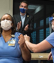 Dr. Audrey Roberson reacts after receiving a COVID-19 vaccine Wednesday from nurse Veronica Nolden at VCU Health. Gov. Ralph S. Northam applauds in the background. Dr. Roberson, a nurse manager of the medical respiratory intensive care unit, was the first front line medical worker at VCU Health to receive the Pfizer vaccine.