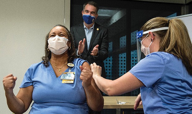 Dr. Audrey Roberson reacts after receiving a COVID-19 vaccine Wednesday from nurse Veronica Nolden at VCU Health. Gov. Ralph S. Northam applauds in the background. Dr. Roberson, a nurse manager of the medical respiratory intensive care unit, was the first front line medical worker at VCU Health to receive the Pfizer vaccine.