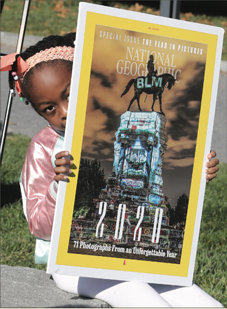 Storie Nzassi, the 7-year-old granddaughter of Delegate Delores L. McQuinn of Richmond, holds
an enlarged copy of the cover of National Geographic Magazine’s January edition featuring a projection of George Floyd’s face
on the statue of Confederate Gen. Robert E. Lee in Richmond. The Monument Avenue statue became a rallying point for protesters against police brutality and racial injustice following Mr. Floyd’s death in May
at the hands of a Minneapolis police officer. Images representing the struggle for civil rights and equality in the United States were projected onto the monument by Richmond artists Dustin Klein and Alex Criqui and photographed by Kris Graves for the cover. The youngster was attending a news conference last Friday with her grandmother at the Virginia Museum of Fine Arts, where Gov. Ralph S. Northam proposed $11 million in state funds be used to transform Monument Avenue.