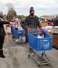 Volunteer Jeff Dean, 53, of North Chesterfield, center, maneuvers among the pallets of fresh fruit and produce where other volunteers fill his grocery cart with food. He then will load the food into one of the hundreds of cars waiting at the Chesterfield Food bank.