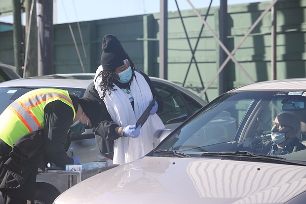 Health teams with carts filled with supplies make their way through a row of vehicles last Friday at the Arthur Ashe Jr. Athletic Center to provide COVID-19 vaccinations to seniors waiting in their cars. Those who were ambulatory went inside the center for their shots.